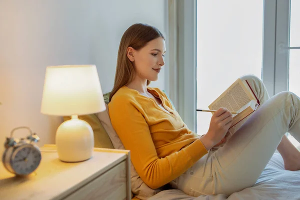 本の虫 リラックスした学生の女の子は 家庭で居心地の良い近代的なベッドルームで座って読書を通して 現代文学を学び 新しい世界を発見し ペーパーバック本を読んでメモを取る 週末のレジャー — ストック写真