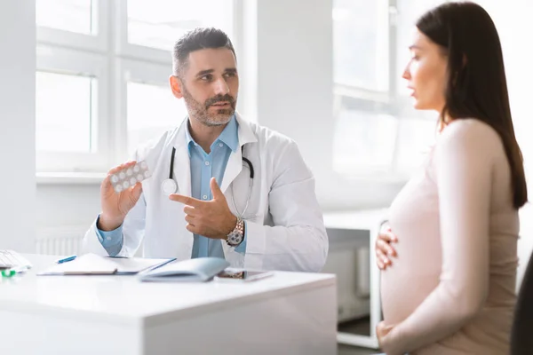 怀孕健康 全科医生向年轻孕妇 与女士预约给药的男产科医生展示药物作为处方药 — 图库照片