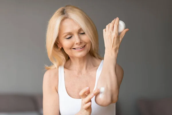 身体护理的概念 快乐的老年妇女在家中抚慰自己的同时 在肘部揉搓润肤乳液 女性使用营养霜 复制空间 — 图库照片