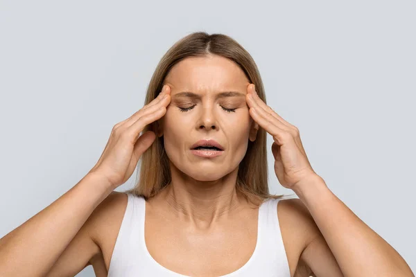 ブロンド中年女性とともに閉じ目こすり寺院で灰色のスタジオの背景 強い頭痛を経験します 片頭痛の種 クローズアップ写真 コピースペース — ストック写真