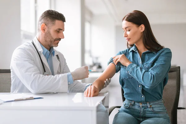 打针时间到了男医生戴着手套 为年轻的女病人注射疫苗 将注射器插入她的胳膊 妇女在现代诊所接种病毒疫苗 — 图库照片