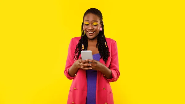 携帯電話を使ったスタイリッシュな黒の女性 サーフィンアプリ黄色いスタジオの背景に立つソーシャルメディアコミュニケーションとデジタル接続を楽しんでいます 技術とガジェット パノラマ — ストック写真