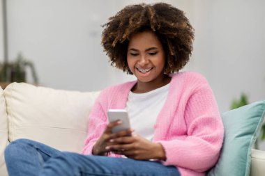 Neşeli, sevimli, çekici, gür saçlı, diş telli, akıllı telefonlu, blog okuyan, sosyal medyada, iç mekanda, fotokopi odasında, yakın çekim yapan Afro-Amerikan kadını.