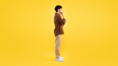 İlginç bir teklif reklamı. Gülümseyen Genç Adam, Chin 'e dokunuyor. Kopya Alanı' na bakıyor. Sarı Stüdyo 'nun arkasında duruyor. İlgilenen adamın yan görüntüsü. Panorama, Tam Uzunluk