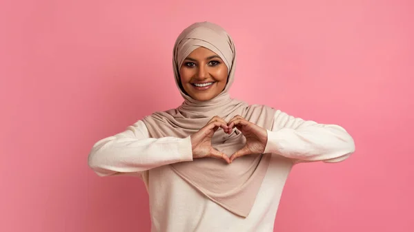爱的概念在相机前展示心形的笑脸 在工作室 复制空间中展示粉红背景时 快乐的年轻伊斯兰女士手拉手靠近胸部 — 图库照片