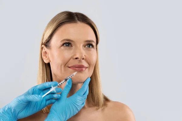 幸せなかなりブロンドの中年女性は彼女の唇に化粧品注射を取得します 顔の若返り手順のためのヒアルロン酸注射 美容室の女性 整形外科 コピースペース — ストック写真