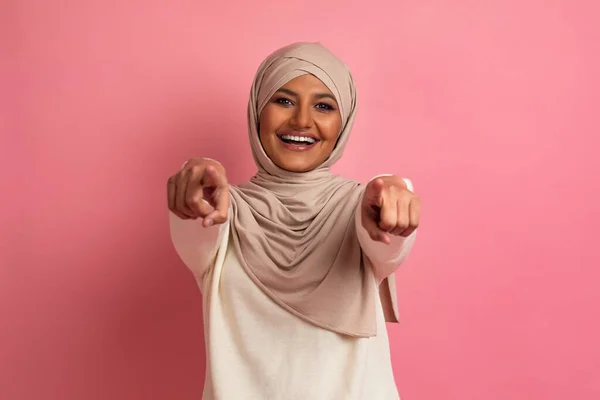 抓到你了喜庆的穆斯林女士在希贾布的相机前指着两个手指 积极的伊斯兰女性头戴头巾指示某人 站在粉红工作室的背景下笑着 复制空间 — 图库照片