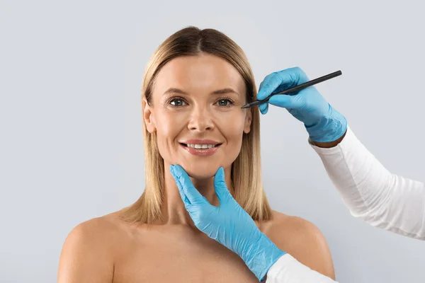 眼底手術 レーザー整形外科 美容師手描画ライン上のペンで中年女性の顔 美しいです陽気なブロンド女性持っていますプラスチック外科でクリニック コピースペース — ストック写真