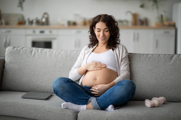 Joven Mujer Embarazada Sonriente Acariciando Barriga Mientras Relaja Sofá Casa — Foto de Stock