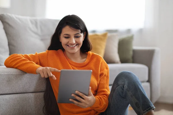 快乐迷人的长发年轻女性 身穿休闲装 坐在地板上 使用数码平板电脑 查看最新的娱乐移动应用程序 复制空间 — 图库照片