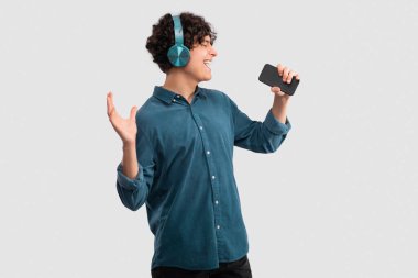 Müzik Teknolojisi ve Gadget 'lar. Kulaklık takan ve mikrofonunu açık gri stüdyo arka planında tutuyormuş gibi yapan ve favori şarkının tadını çıkaran genç adam.
