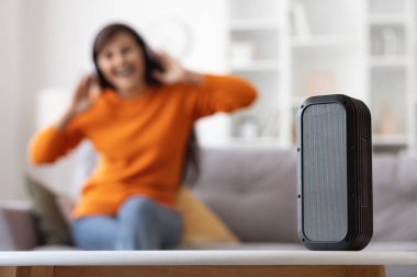 Modern kablosuz müzik köşesine odaklanın. Bu sırada tanınmayan bir kadın müzik dinlerken, favori şarkının tadını çıkarırken, evdeki koltukta otururken. Ev işleri ve aletler.