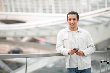 Her zaman bağlı. Cep telefonu kullanan turist mesajlar gönderiyor ve aile ile seyahat haberleri paylaşıyor modern havaalanında bavullarıyla kameraya bakıyor. Seyahat İletişim Konsepti