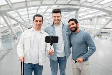 Heyecanlı Kaşifler. Cep telefonunda Selfie Yapan Üç Gezgin İnternette Mutlu Seyahat Anları Paylaşıp Modern Havalimanı 'nda Kucaklaşan Üç Gezgin. Teknoloji ve Turizm Konsepti