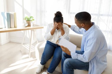 Depresyon, endişe konsepti. Genç siyahi adam psikologu ağlayan bayanı teselli ediyor artı beden, depresyonda olan İspanyol kadın danışmanıyla terapi seansına katılıyor, fotokopi odası, klinik içi.