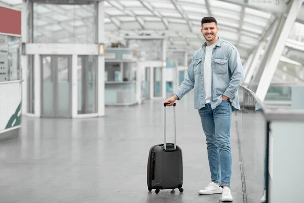 给Globetrotter的旅行优惠 携带手提箱行李的旅客站在机场室内对着相机微笑 年轻乘客等待飞行的全长镜头 复制空间 — 图库照片