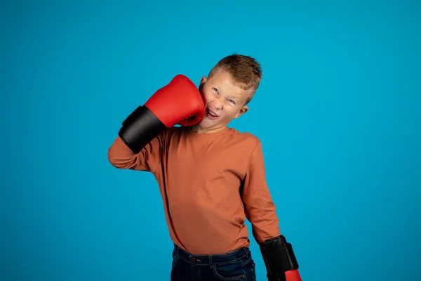 疯狂运动 可笑的小男孩 戴着拳击手套 冲着自己的脸 快乐的未成年男孩儿 在蓝色工作室的背景下 一边站着一边玩一边玩乐 复制空间 — 图库照片