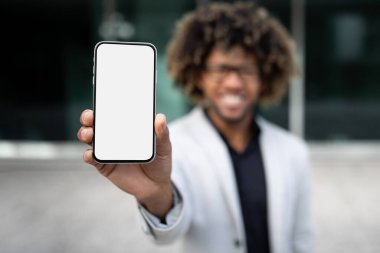 Yeni iş uygulaması. Siyah işadamı cep telefonunu boş ekran ile gösteriyor, cep telefonu uygulaması veya finans, seçici odak, modelleme için web sitesi öneriyor