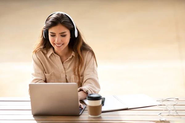 キャンパスでオンラインレッスン ヘッドフォンで陽気な若いアジアの女性の学生は コーヒー 屋外のカップとテーブルの大学でコンピュータでチャット 遠隔で勉強し 教育のための装置 試験準備 — ストック写真