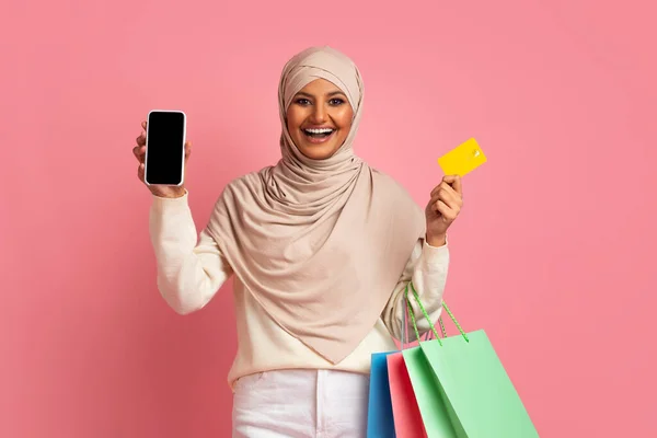 购物应用程序 快乐的穆斯林女性拥有智能手机 购物袋和信用卡 用空白屏幕在Hijab展示手机微笑伊斯兰女性 推荐网上商店 — 图库照片
