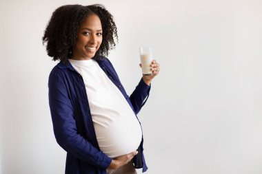 Neşeli bin yıllık Afro-Amerikan hamile kadın büyük göbeği olan gri duvar arkasında bir bardak süt tutan kadın. Çocuk beklentisi, sağlık, evde diyet, reklam ve teklif