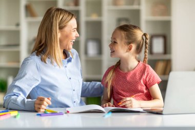 Anne ve küçük tatlı kızı ödevlerini yaparken eğleniyorlardı mutlu bir anne ve kız çocuğu evde masasında oturuyorlardı ve birbirlerine gülümsüyorlardı.