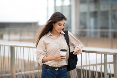 Çalışmak için modern iletişim. Sırt çantalı mutlu Asyalı kız öğrenci, bir fincan kahve servisi, açık havada akıllı telefondan sohbet. Günlük ve uygulama, öğrenme aygıtı, eğitimden uzaklaşma