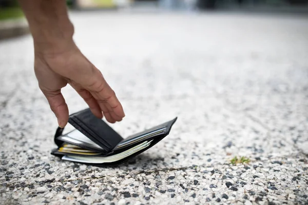 Closeup view of black man picking up lost wallet full of money banknotes on city street, selective focus, empty space. Lost money concept
