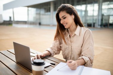 Asyalı genç bir kız öğrenci, üniversitede bilgisayar okuyan bir öğretmen, dışarıda kahve fincanı ile kampüste çalışıyor. Uzaktan ders teknolojisi, modern eğitim online, sınav hazırlığı