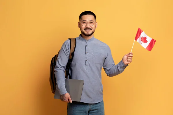 Χαμογελαστός Ασιάτης Καναδική Σημαία Και Laptop Χέρια Ποζάροντας Στο Κίτρινο — Φωτογραφία Αρχείου