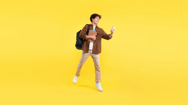 快乐学生的家伙使用智能手机 访问教育应用程序学习的过程 网上冲浪和享受在线娱乐电话 运行在黄色工作室背景 — 图库照片
