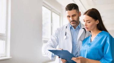 Sağlık hizmetleri ekip çalışması. Erkek doktor ve asistan hastaların sağlık geçmişini inceliyor, hastane ofisinde tartışıyor, fotokopi çekiyor. Hasta bakımı koordinasyonu