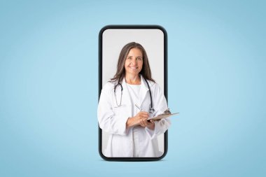 Modern tıp hizmetleri. Stetoskop ve not panosuyla hasta için reçete yazan, beyaz üniformalı, kıdemli, neşeli doktor kadın, büyük bir cep telefonu ekranına bakıyor.
