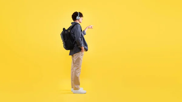 背带耳机听音乐 按隐形按钮或在黄色工作室背景上展示自由空间的年轻人的侧视图 — 图库照片