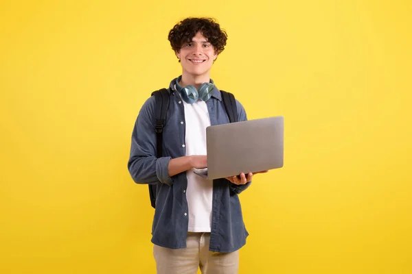 学問的成功 幸せな学生の男はノートパソコンのコンピュータのウェブサーフィンを入力し 黄色のスタジオの背景の上に立ってオンライン学習 カメラに微笑む 教育とインターネット技術の概念 — ストック写真