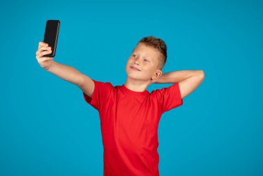 Smartphone 'da selfie çeken yakışıklı küçük bir çocuğun portresi, Mobile Phone' da çocuk pozu veren sevimli beyaz erkek çocuk, Mavi Stüdyo Arkaplanı, Bedava Alan