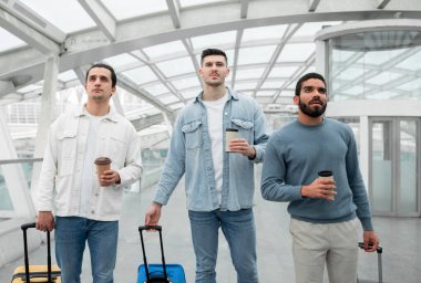 Uçuş Gecikmesi. Seyahat bavullu üç ciddi gezgin ve modern havaalanı terminalinde duran çıkış tahtasına bakan kağıt kahve bardakları. Tatil Yolculuğu Rutin Konsepti