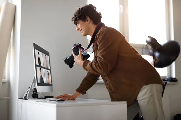 Creative job. Happy young man photographer in casual outfit working at photo studio office, using digital camera and pc, checking photo shoot, side view