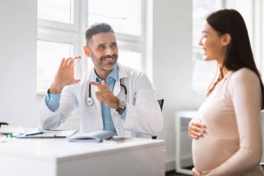 Vitamin reçetesi. Klinikte kontrol edildikten sonra hamile kadına reçete yazan gülümseyen erkek doktor. Dost canlısı erkek terapist şişeyi haplarla ya da vitaminlerle gösteriyor.