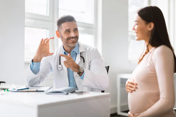 维生素处方 在诊所检查后 微笑着给孕妇开处方的男医生 友善的男性治疗师 指着装有药丸或维生素的瓶子 — 图库照片