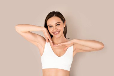 Yüz bakımı rutini. Güzel, gülümseyen, beyaz iç çamaşırı giyen beyaz tenli bir kadın. Yüzünün yanında el ele tutuşuyor. Güzel, pürüzsüz, parlak bir ten rengi, bej renkli bir stüdyo geçmişi var.