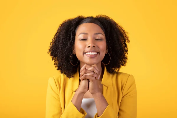 快乐的微笑着的黑人女士做着祷告的姿势 许个愿 祈求奇迹 孤零零地站在黄色工作室的背景上 人类的情感 — 图库照片