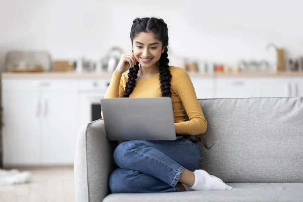 Young Smiling Indian Woman Relaxing With Laptop On Couch At Home, Beautiful Happy Eastern Lady Watching Movies Or Browsing Internet On Computer While Resting On Sofa In Living Room, Copy Space