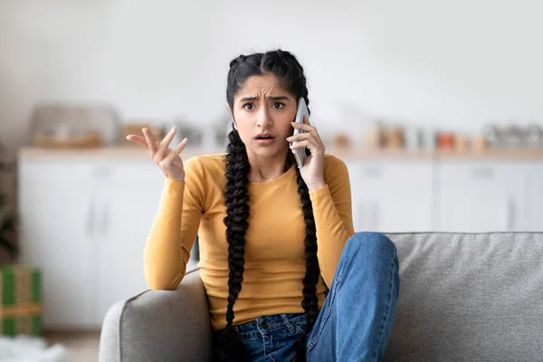 打错电话了图片说明沮丧的印度女性在家里用手机交谈时 紧张的东方女性在客厅里坐在沙发上与令人不快的手机交谈时的形象 — 图库照片