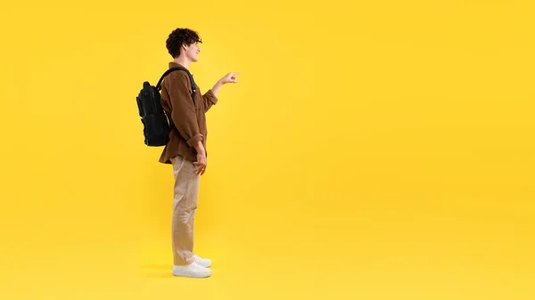 在空旷的文字空间 用背包向学生展示手指 展示伟大的教育机会或课程广告站在黄色工作室的背景下 侧视图 — 图库照片