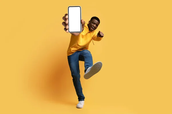 年轻帅气帅气的黑人小伙子嬉皮士展示智能手机与白色空白屏幕 大拇指向上和鞋底 孤立在黄色工作室背景 数字生活 现代技术 — 图库照片