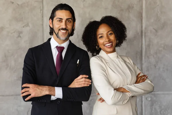 Cheerful attractive successful middle eastern middle aged man and black young woman managers standing back to back with arms crossed on chest, smiling at camera, office interior. Partnership concept