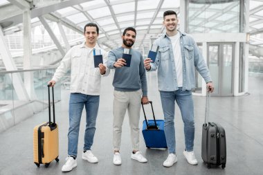 İş Seyahat Dostları. Mutlu Genç Gezginler, havalimanında kalkış terminalinde durmakta olan pasaportlarını ve biniş kartlarını gösteriyor. Ucuz Biletler reklamı. Tam Uzunluk