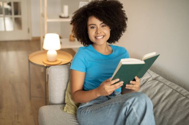 Hafta sonları tek başına rahatla. Milenyum kıvırcık kıvırcık, kitap okuyan, rahat oturma odasındaki kanepede boş vakitlerin tadını çıkaran bir kadın. Akşamları hobiler, eğitim ve bilgi.