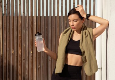 Spor giyimli, spor kıyafetli, havluyla ve bir şişe suyla antrenmandan yorgun düşmüş, beyaz bir bayan. Spor, antrenmanlara ara vermek, kilo vermek, şehirde sağlık hizmetleri